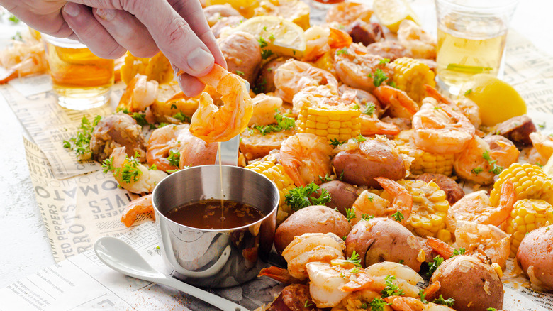 Close up of Instant Pot Shrimp Boil and a hand dipping shrimp in seasoned butter