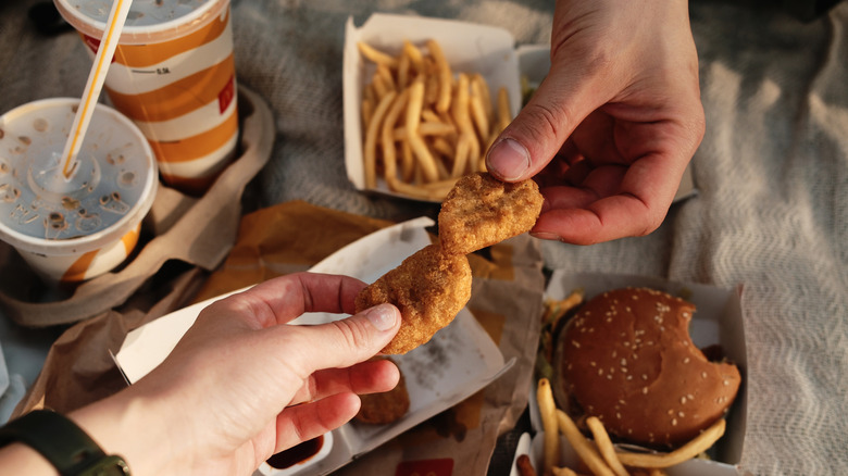 Two hands sharing fast food items including nuggets, burger, and drinks