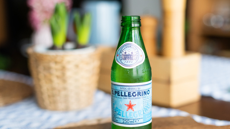 a bottle of San Pellgrino water on a wooden table with blurred flowers and ornaments in the background