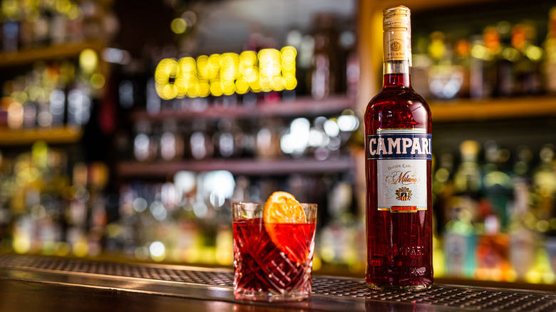 A bottle of Campari next to a cocktail on a bar