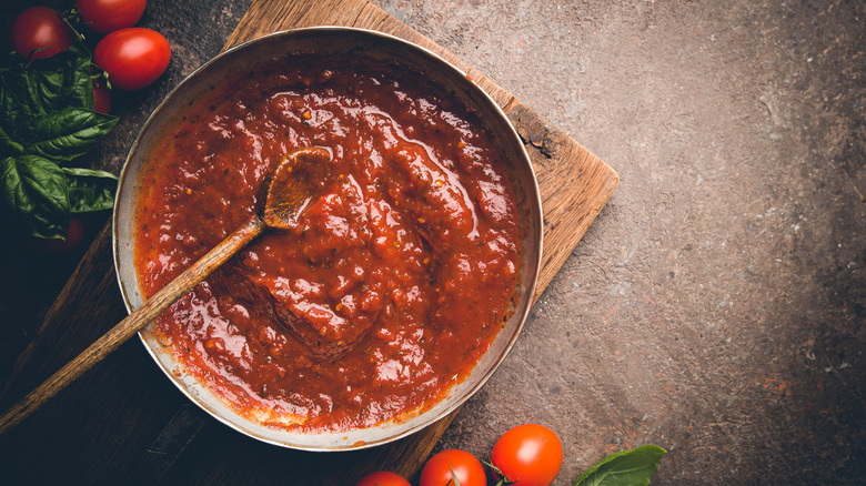 tomato sauce in a large pot with a wooden spoon and fresh tomatoes on the counter 