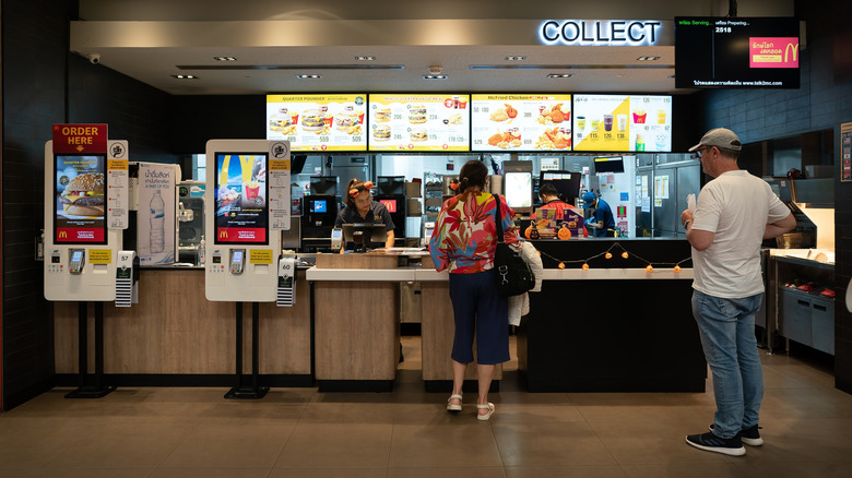 Two people stand in line at a McDonald's register waiting to order their food and pay.
