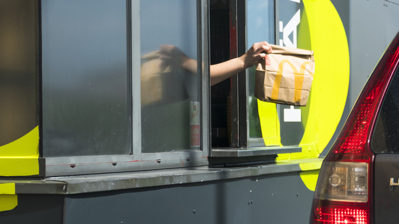 A McDonald's worker handing a bag out of the drive-thru window into a black car.
