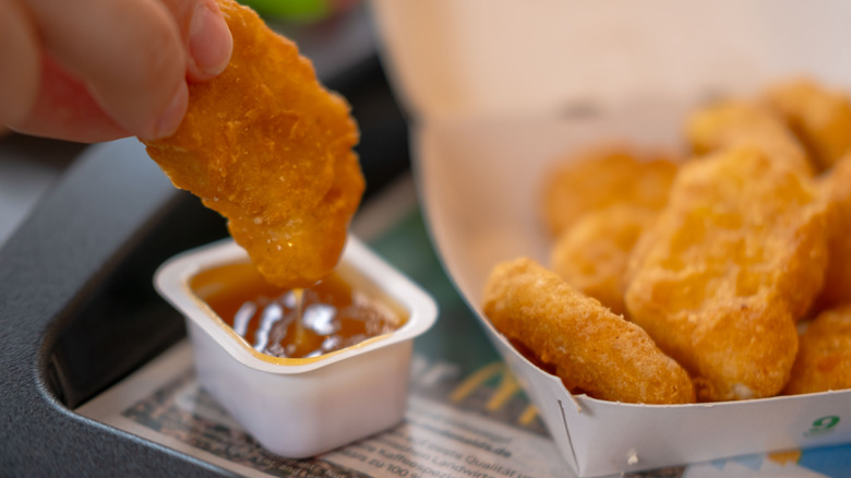 Fingers dipping a McDonald's chicken nugget in sauce, next to a tray of McDonald's nuggets.