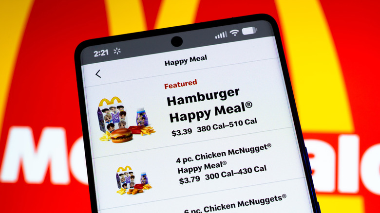 A phone with the McDonald's mobile order app on the screen in front of a McDonald's sign.
