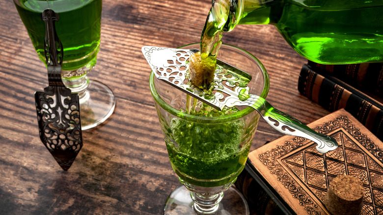 Absinthe being poured over a sugar cube on an ornate slotted spoon into a glass