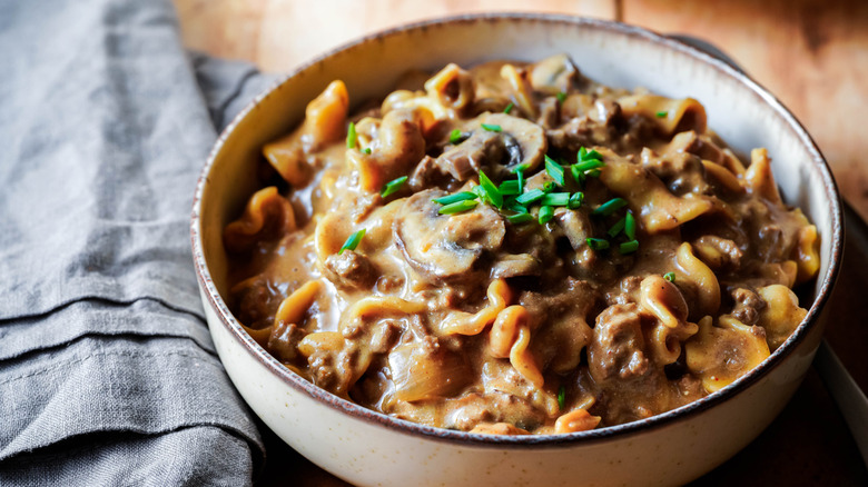 Bowl of beef stroganoff on a wooden table with a gray cloth napkin