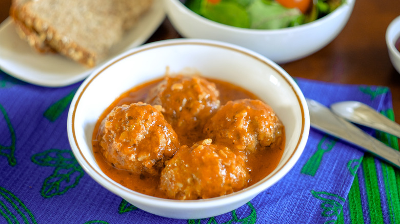 Bowl of porcupine meatballs on a table with bread and salad in the background