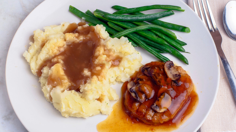 White plate containing Salisbury steak topped with mushroom gravy, mashed potatoes with gravy, and green beans