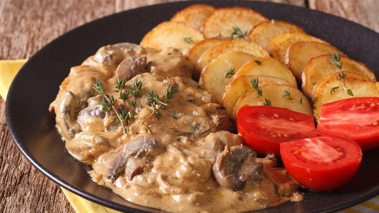 Cut-up steak Diane with potatoes and tomatoes on a black plate