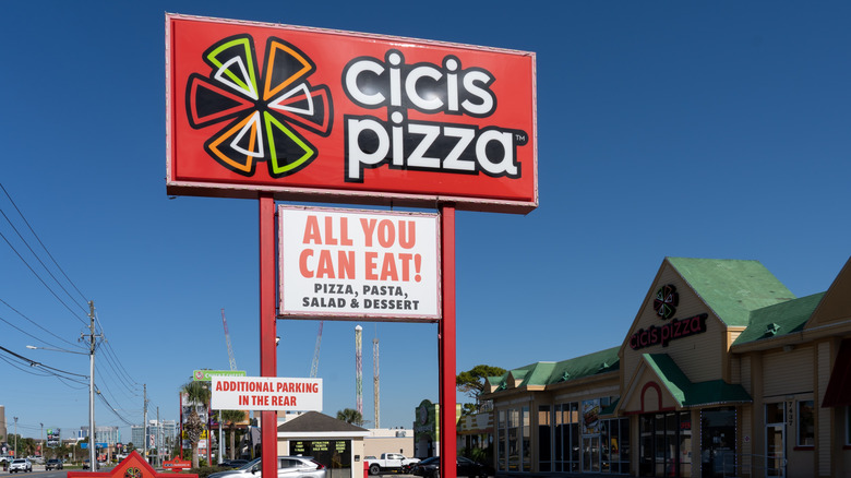 A red outdoor signage for Cicis Pizza with the building visible on the side