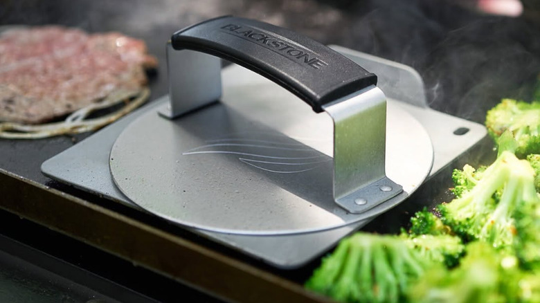 A Blackstone burger press next to a burger on a griddle