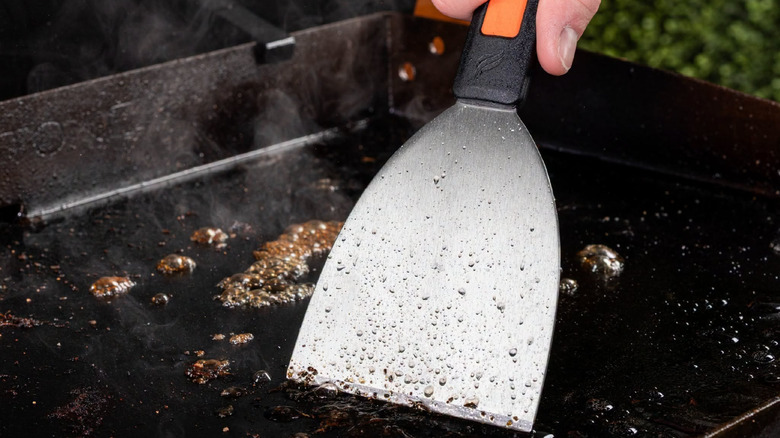 A metal scraper for the Blackstone being scraped on a grill