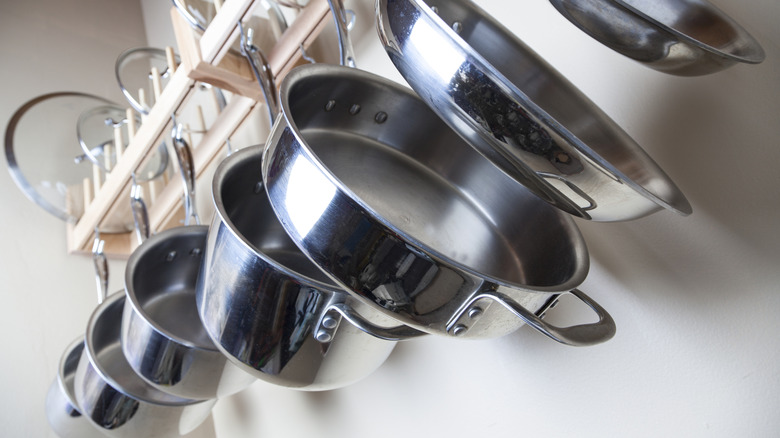 several stainless steel pots hanging from white rack