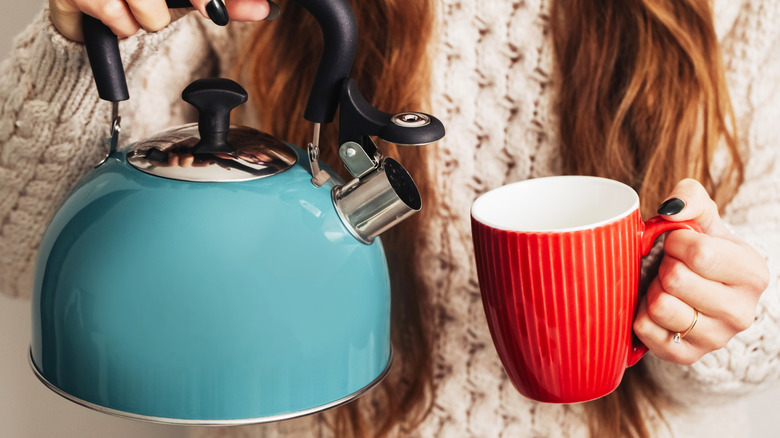 woman holding blue rtea kettle and red mug