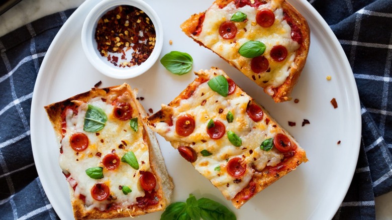 sliced pepperoni French bread pizza on a white plate with a side of chili flakes