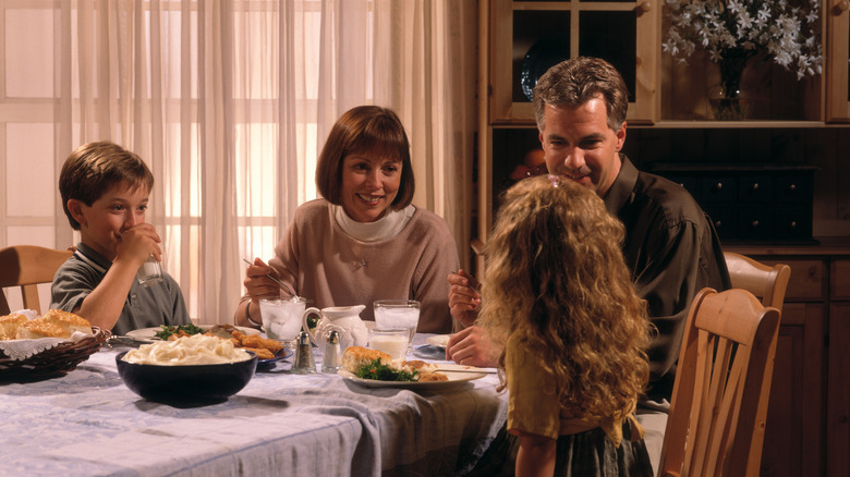 family of four sitting around the dinner table dressed in 1990s clothing
