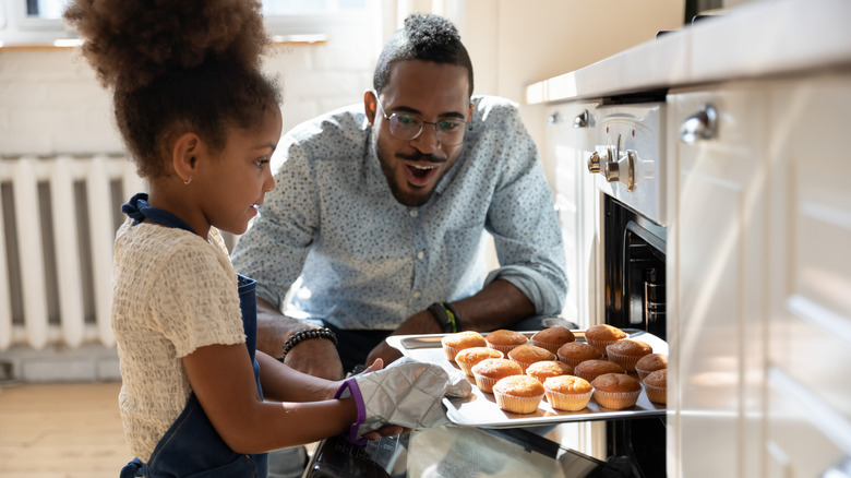 Man watches kid take muffins out of oven