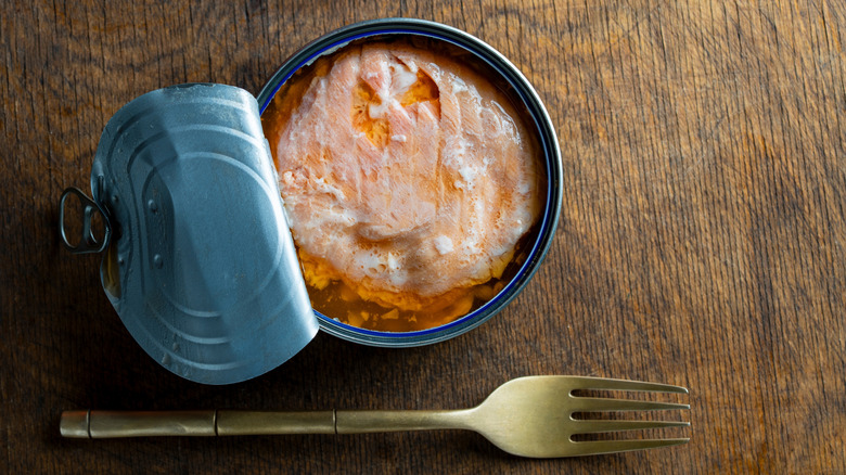 Open can of salmon on a table with a fork