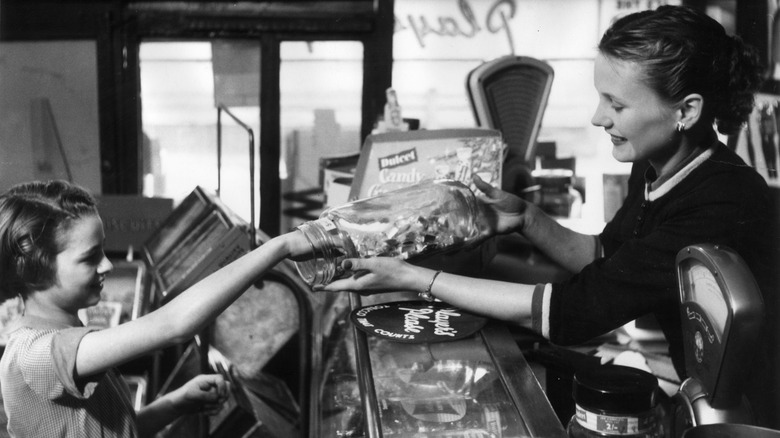 Vintage photo of a girl being served candy from glass jar over the counter in a sweet shop