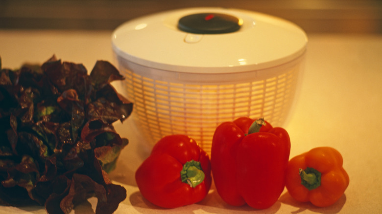 white salad spinner on a counter with lettuce and red bell peppers