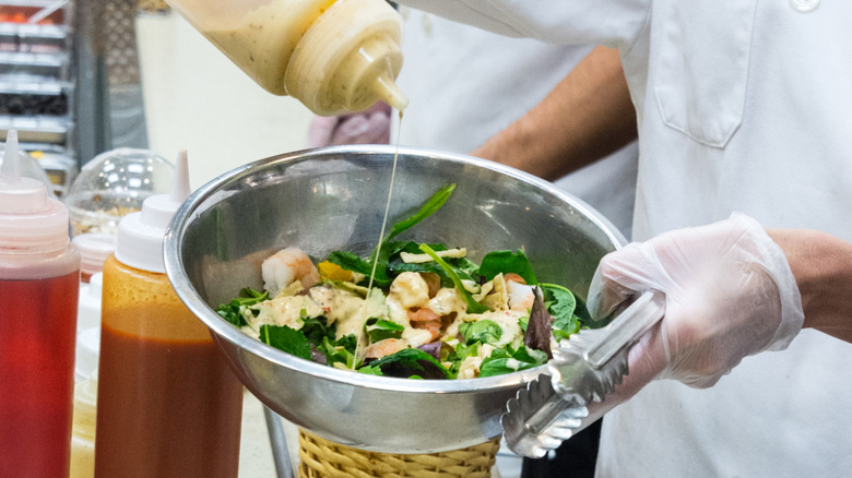 person pouring salad dressing onto a salad