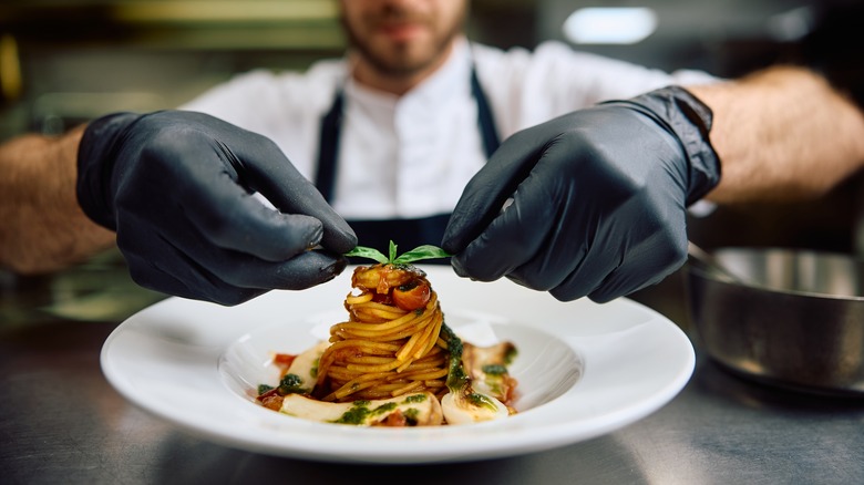 Chef finishing a pasta dish with fresh basil