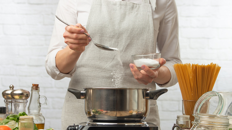Person in kitchen apron salting pot of pasta water