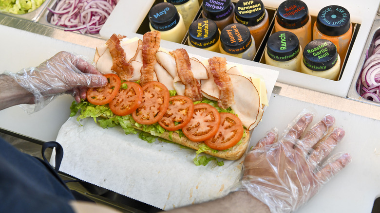 Sandwich artist placing tomato slices on sub at Subway