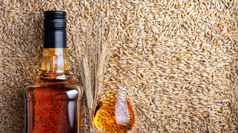 Bottle and glass of bourbon against background of wheat grains