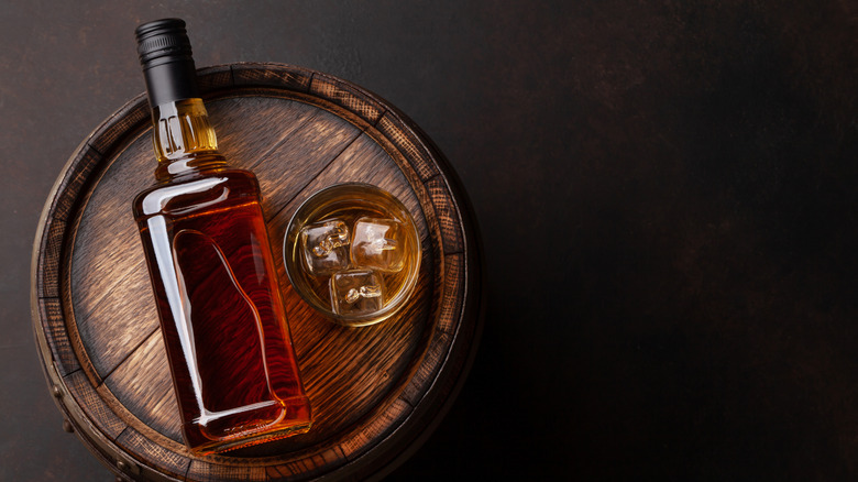 Bourbon bottle on its side on barrel with glass of bourbon and ice