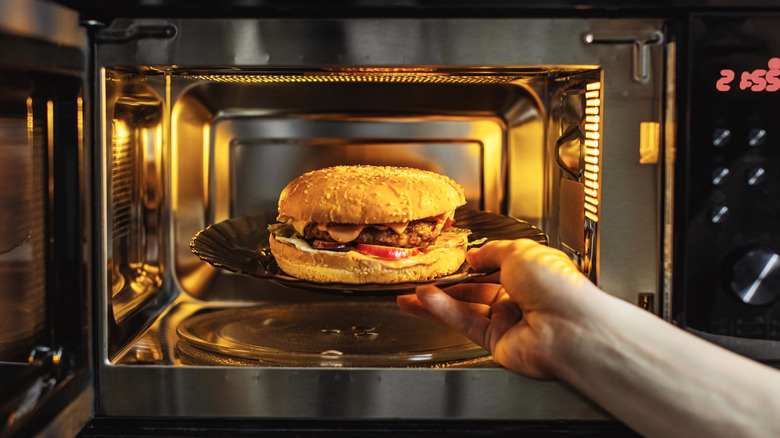 Hand putting cheese burger into a microwave