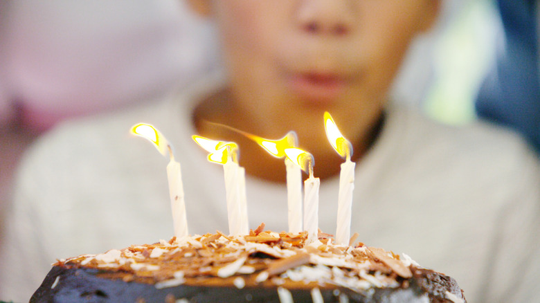 close-up of the top of a cake with birthday candles, a child's face blurry in the background