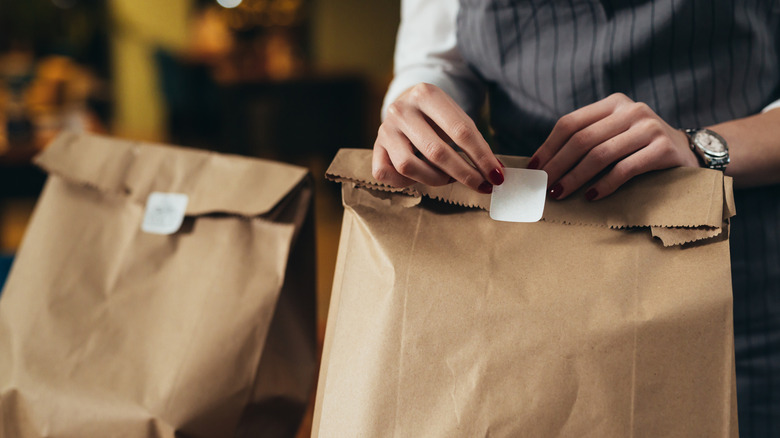 a woman's hands placing a seal sticker onto a brown paper bag package