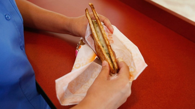 Person holds partially wrapped flatbread sandwich from Dunkin' Donuts in hands.