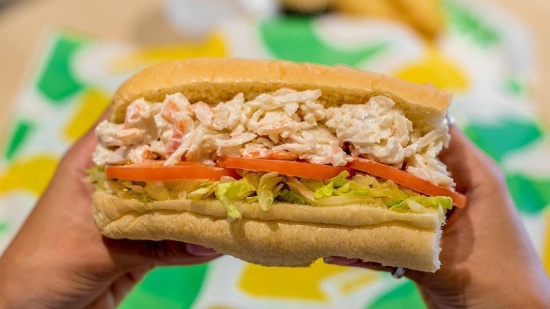 Two hands hold Subway's Seafood Sensation topped with lettuce and tomato.