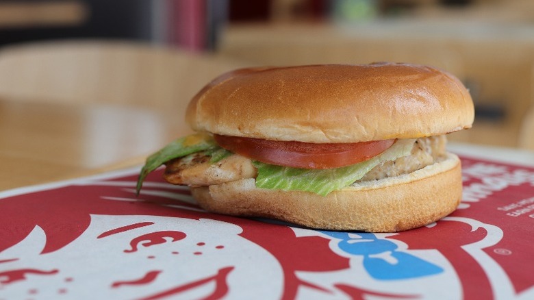 Wendy's Grilled Chicken Sandwich rests on top of branded table with lettuce and tomato peeking out from edge of the bun.