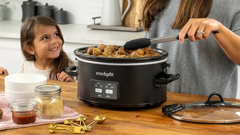 Young girl smiling up at mom while making a slow cooker meal