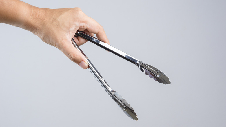 Hand holding silver serving kitchen tongs for picking food on white background