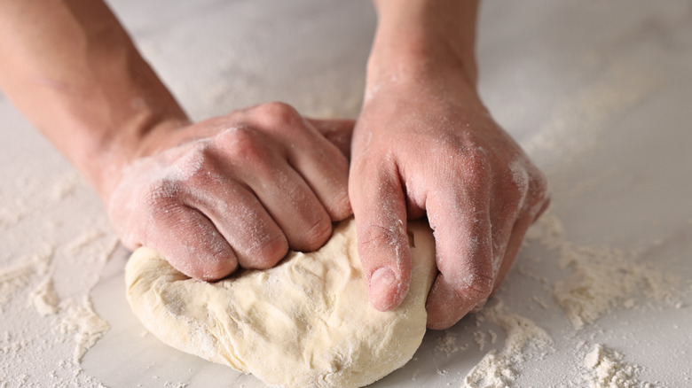 A close-up of hands kneading dough on a marble surface