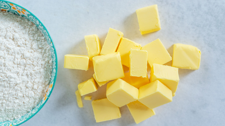 Cubes of yellow butter next to a bowl of flour