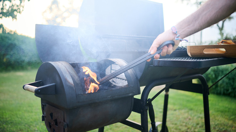 Man with tongs moving something in a smoker