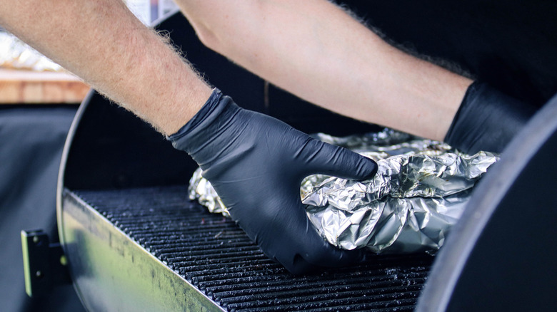 Mans hands placing foil wrapped ribs in a smoker