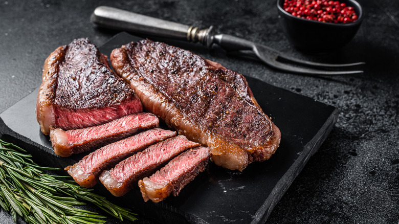 Two cooked steaks on black slate, one sliced