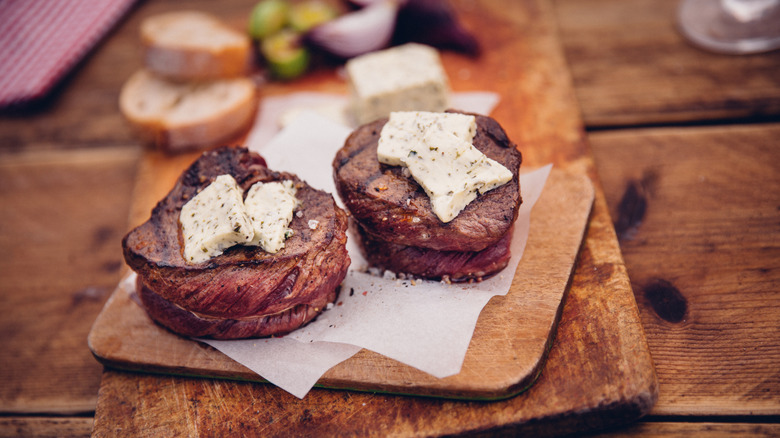 Two filets resting on a board with herbed butter