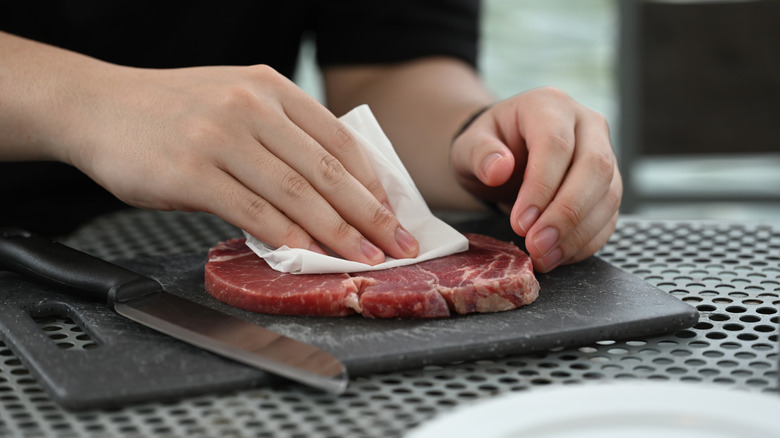 Person's hands using a paper towel to pat a thin steak drt