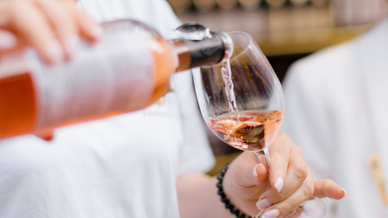 Person pouring rose wine in a glass.