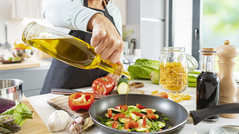 pouring oil into a skillet with veggies