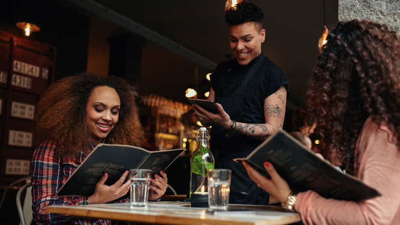 Two diners reading menus while waiter stands next to table
