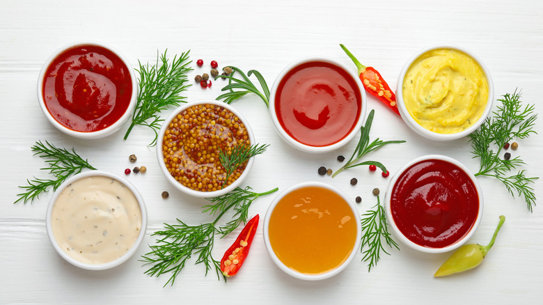 An array of condiments in white dishes with fresh herbs
